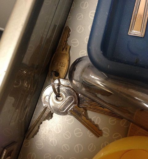 A photograph of some keys wedged behind the corner of a plastic tub on what could be a kitchen counter.