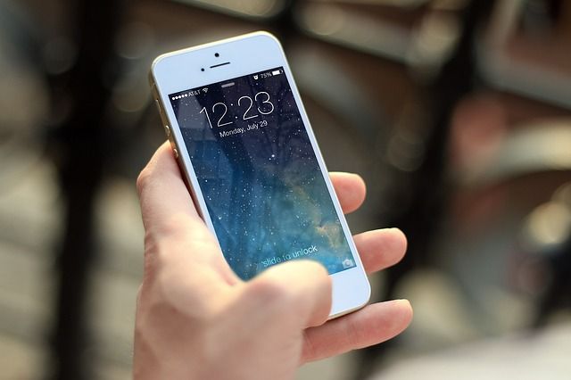 A stock photograph of a hand holding a white iPhone, displaying the lock screen and the time 12:23.