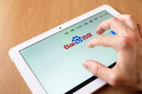 A person's hand poised over a tablet showing the Baidu search engine homepage.